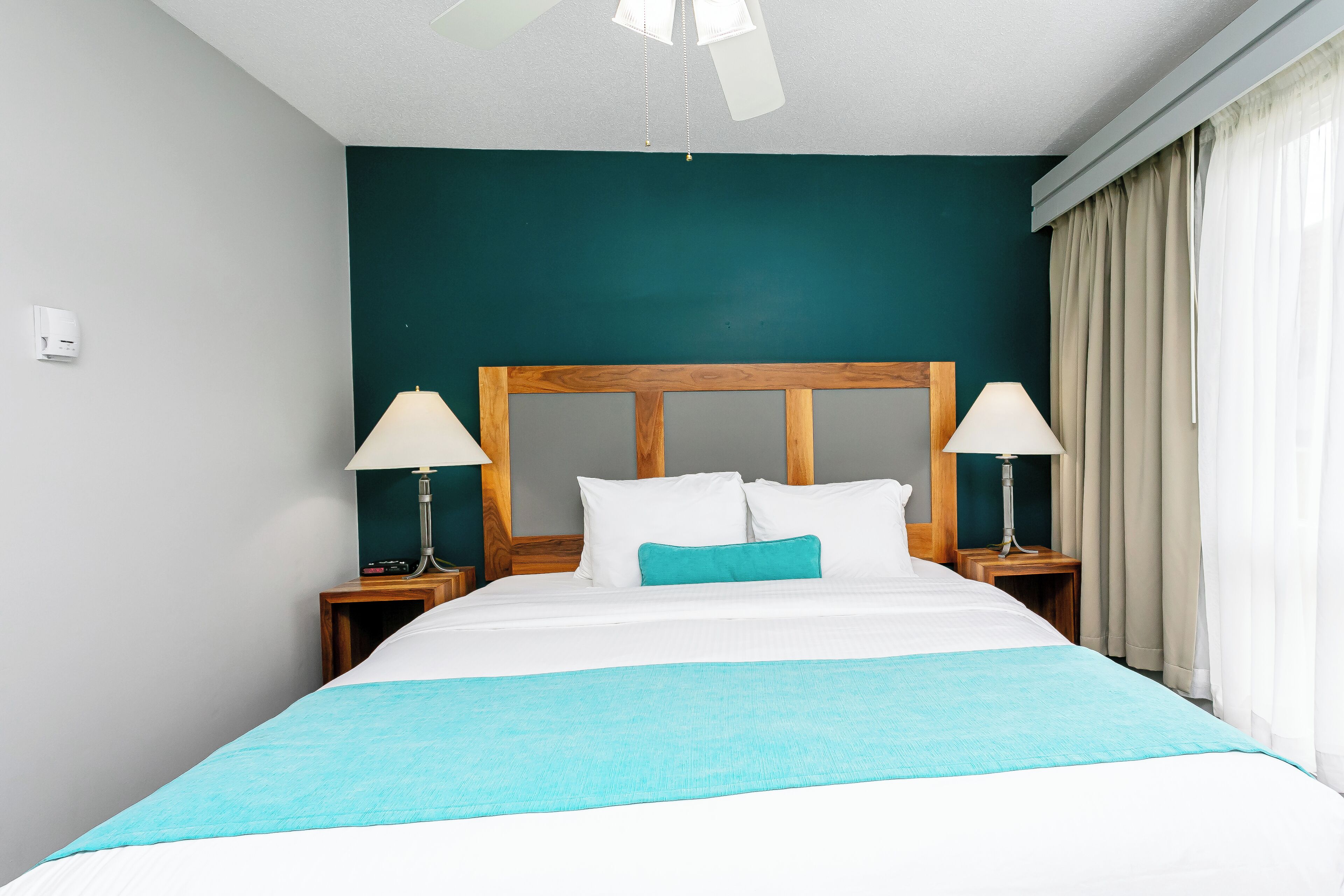 A neatly made bed with a wooden headboard, two bedside tables with lamps, and a teal accent pillow.