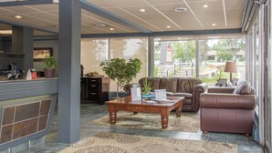 A spacious lobby with a reception desk, leather sofas, a coffee table with papers, and large windows offering a view of the outdoors.