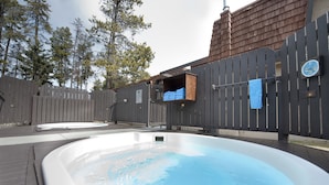 A hot tub in a backyard with a wooden fence, a clock, and a small shed.