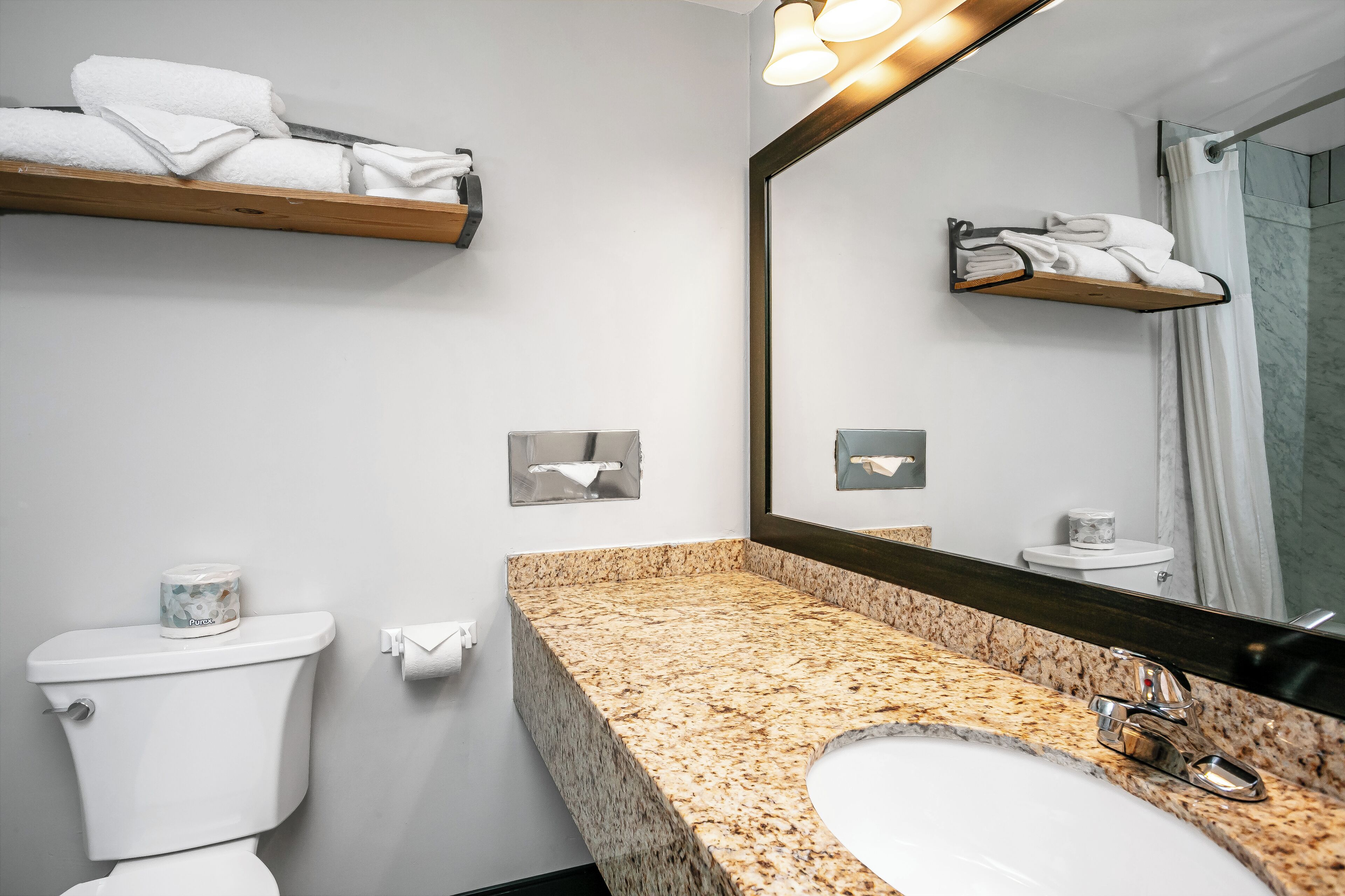 A bathroom with a toilet, sink, mirror, towel rack, and a roll of toilet paper.