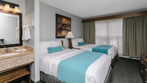 A hotel room with two beds, a bathroom with a sink, and a large window with curtains.