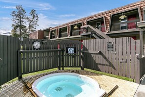 A wooden deck with a hot tub, a fenced area, and a building with numbered rooms.