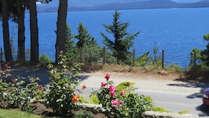 A road with a flower bed in the foreground and a view of a lake and mountains in the background.