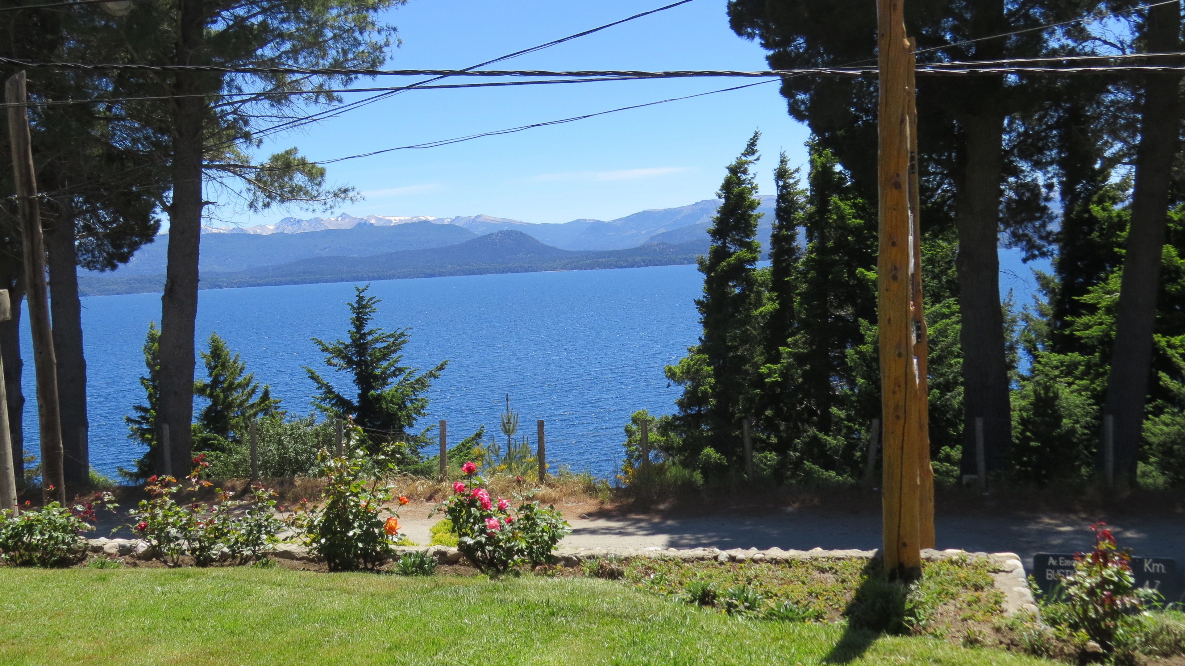 Aussicht auf einen See mit Bergen im Hintergrund, umgeben von Bäumen und einem Garten mit Blumen.