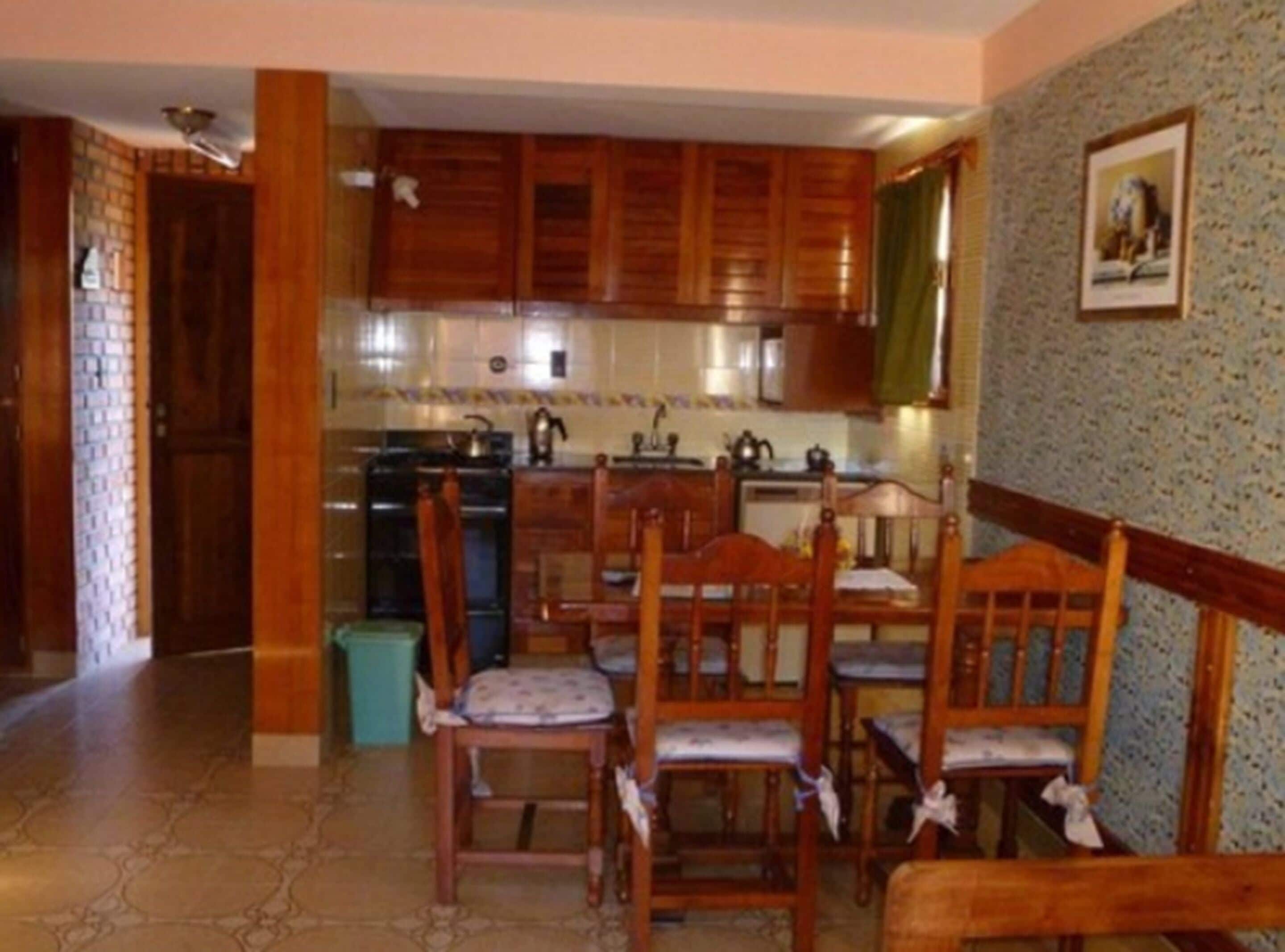 A compact kitchen with wooden cabinets, a dining table with chairs, and a tiled backsplash.
