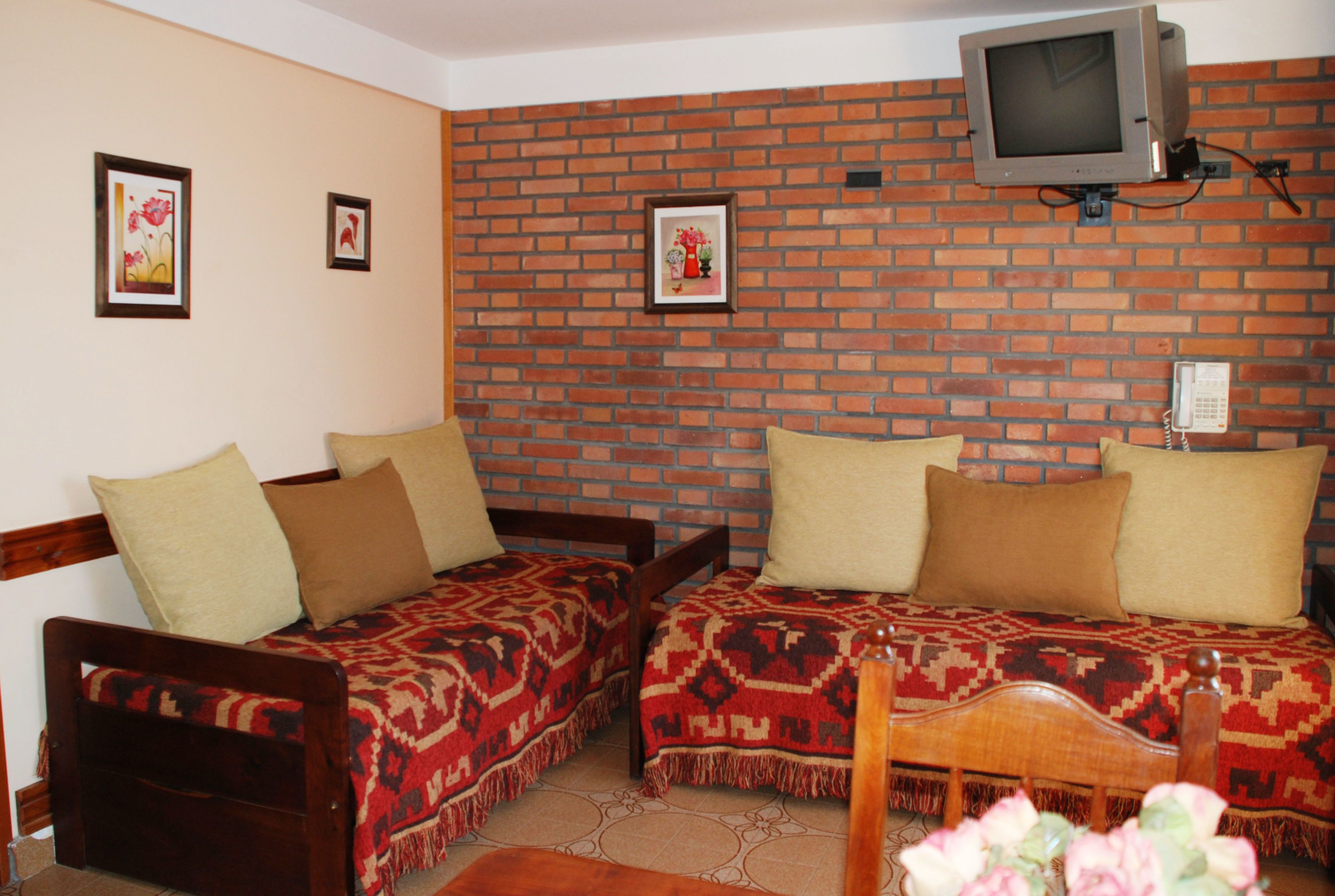 Una habitación con dos camas de madera, una pared de ladrillo y un televisor sobre las camas.