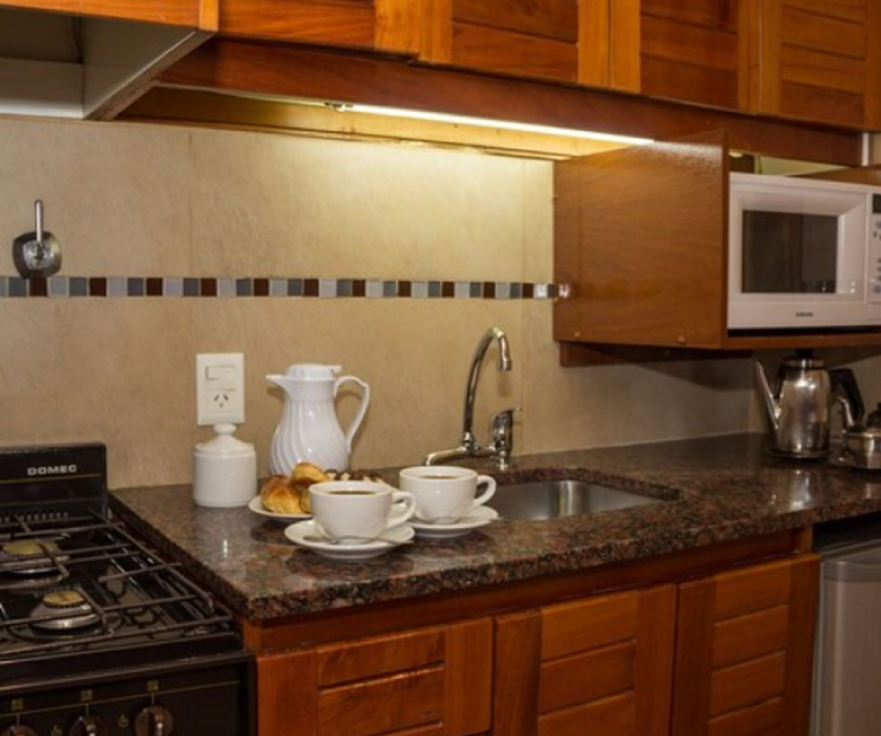 Een keuken met houten kastjes, een gasfornuis, een magnetron en een spoelbak.