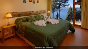 A bedroom with a large bed, two bedside lamps, a wooden headboard, and a view of the sea.