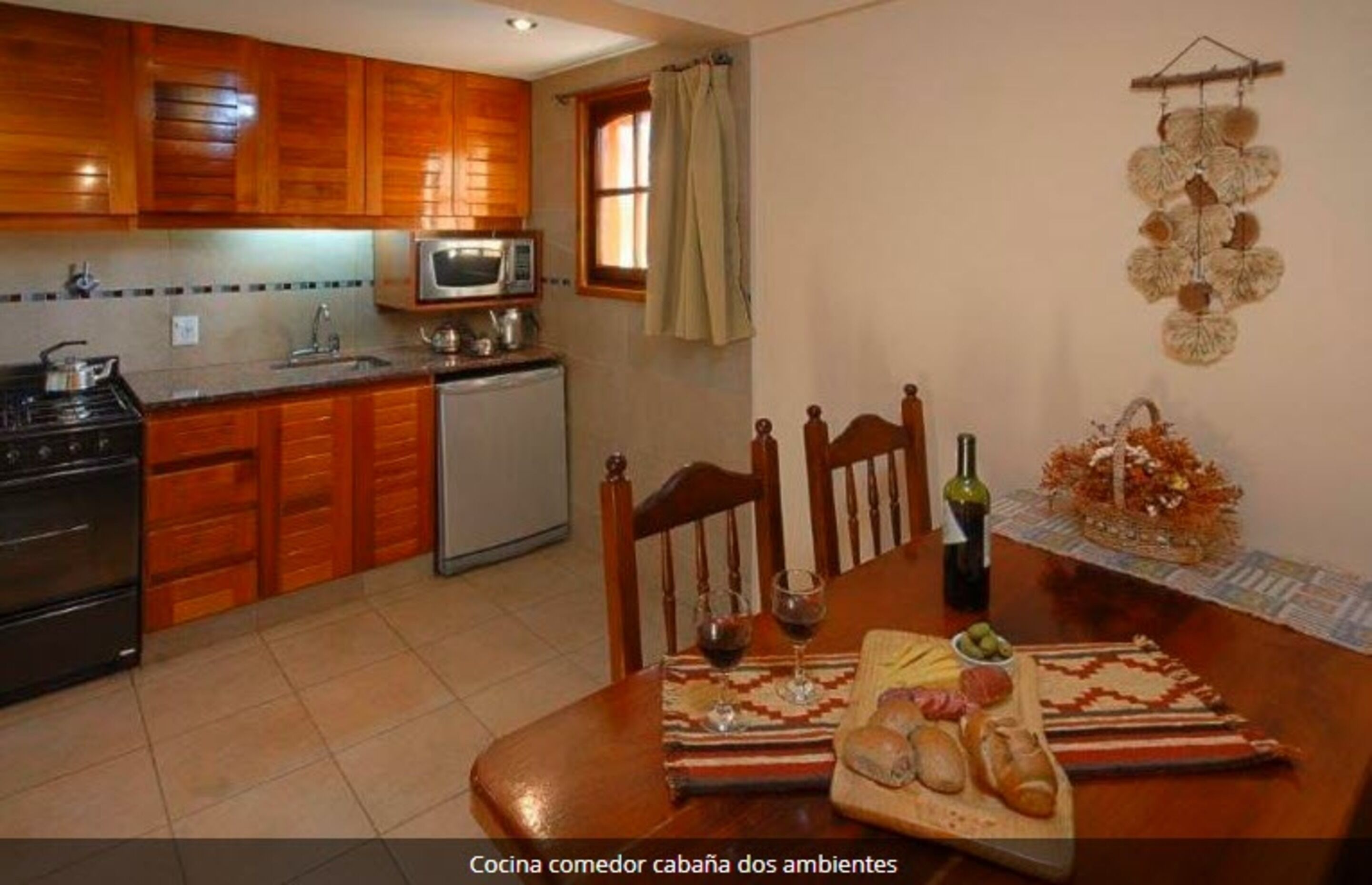 Une cuisine avec des meubles en bois, un four à micro-ondes, un évier et une table à manger, sur laquelle sont disposés du pain, du fromage et des verres à vin.