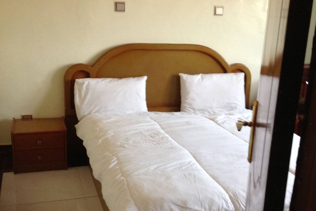 A neatly made bed with white linens in a room with a wooden headboard.