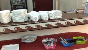 A buffet setup with stacks of white plates, bowls, and utensils on a table with a decorative border. - Nikki Hotel (Niamey)