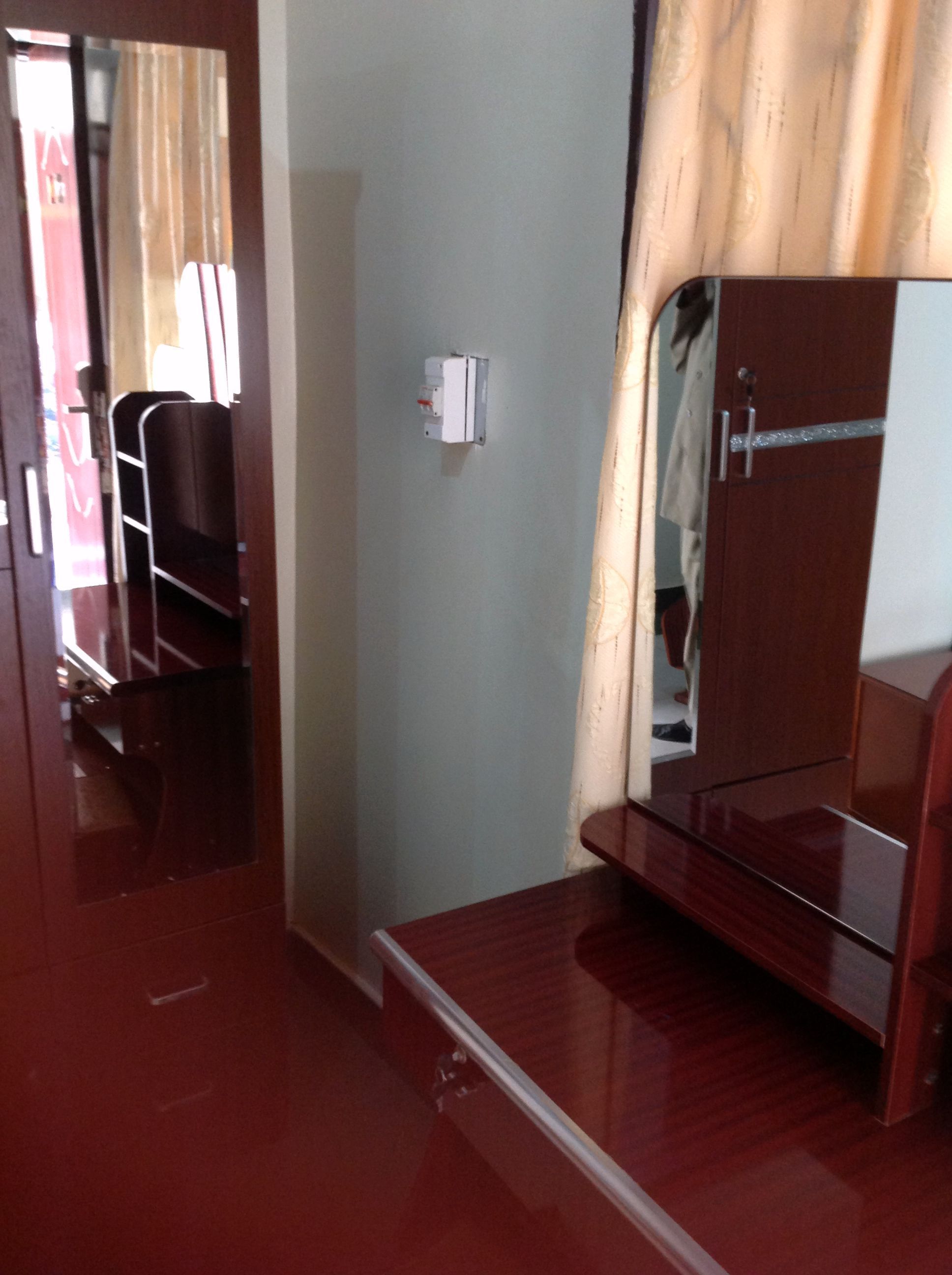 A compact room with a wooden wardrobe, a small table, and a mirror.
