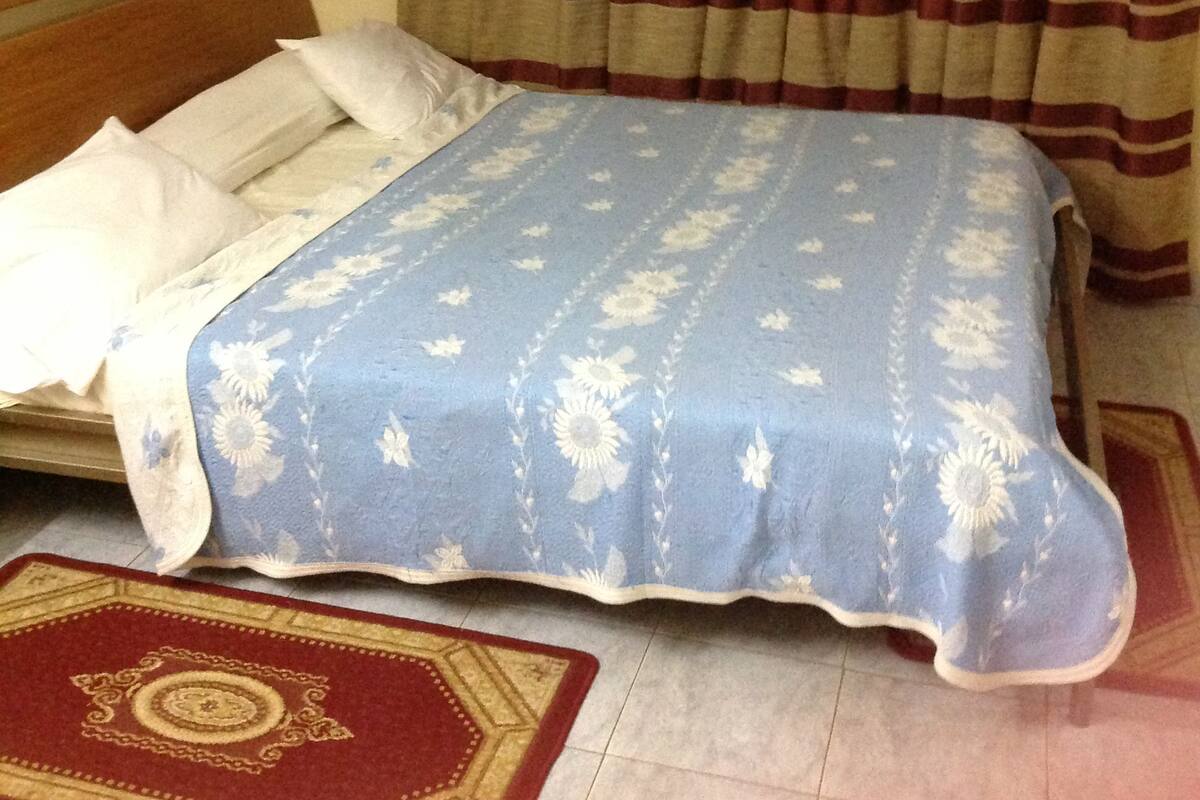 A bedroom with a bed, a red and beige striped curtain, and a blue floral bedspread.