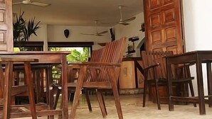 A wooden dining area with chairs and tables, a ceiling fan, and a view of the outdoors. - Hôtel Aurore (Lomé)