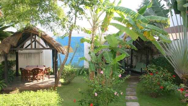 A garden with a thatched-roof structure, a stone pathway, and lush greenery. - Hôtel Aurore (Lomé)