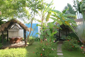 A garden with a thatched-roof structure, a stone pathway, and lush greenery. - Hôtel Aurore (Lomé)