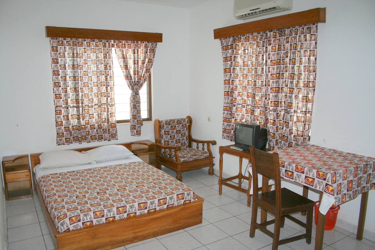 A room with two beds, a chair, a table with a TV, and curtains.