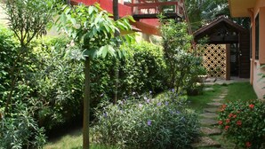 A garden with a stone pathway, lush greenery, and a wooden structure with a balcony. - Hôtel Aurore (Lomé)