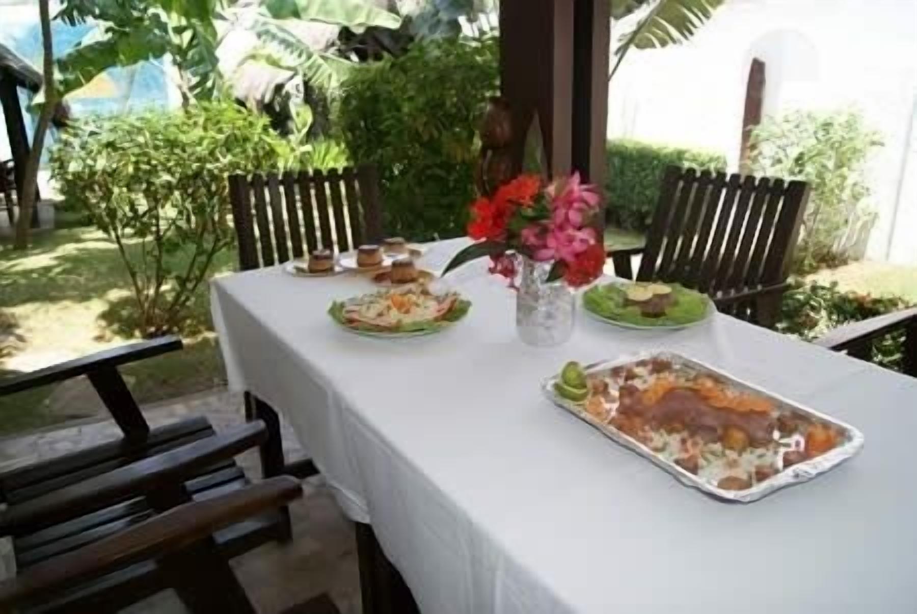 Une table dressée à l’extérieur, avec différents plats, un vase rempli de fleurs et un banc.