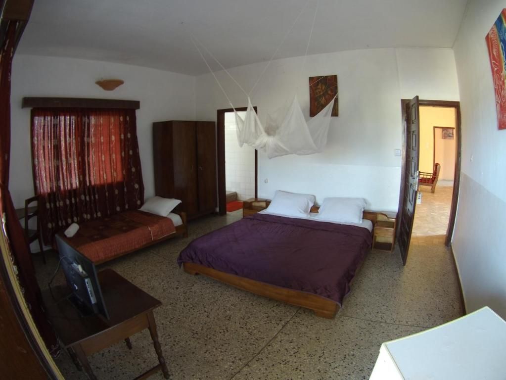Une chambre à coucher avec un lit, un bureau et une chaise. On y trouve également une armoire et une porte qui donne sur une autre pièce.