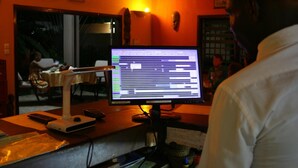 A hotel reception desk with a computer monitor displaying a booking interface, a desk lamp, and a chair. - Hôtel Aurore (Lomé)
