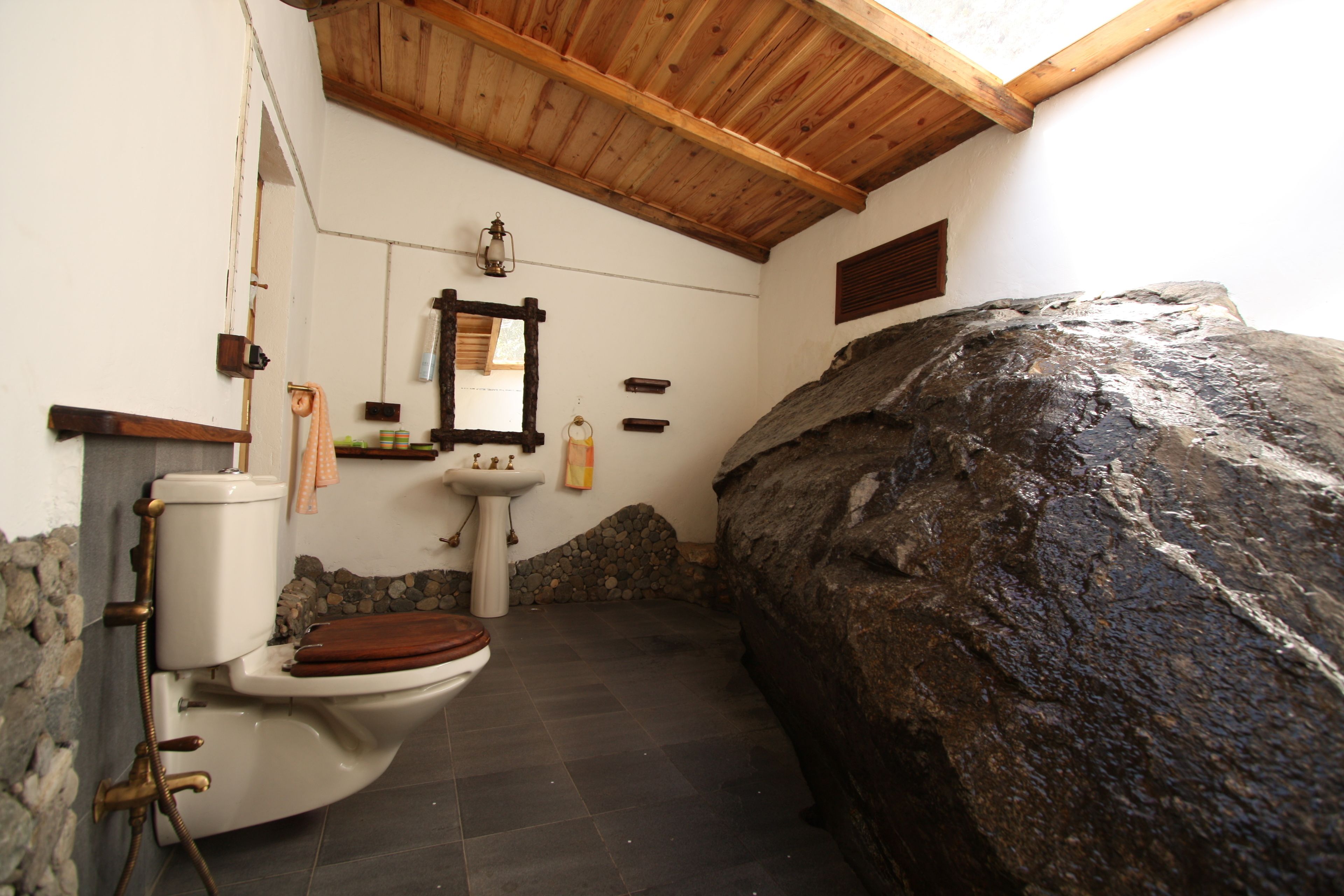 A bathroom with a stone wall, a wooden ceiling, a toilet, a sink, and a mirror.