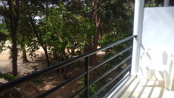 A balcony with a metal railing overlooking a garden with trees and a sandy ground.