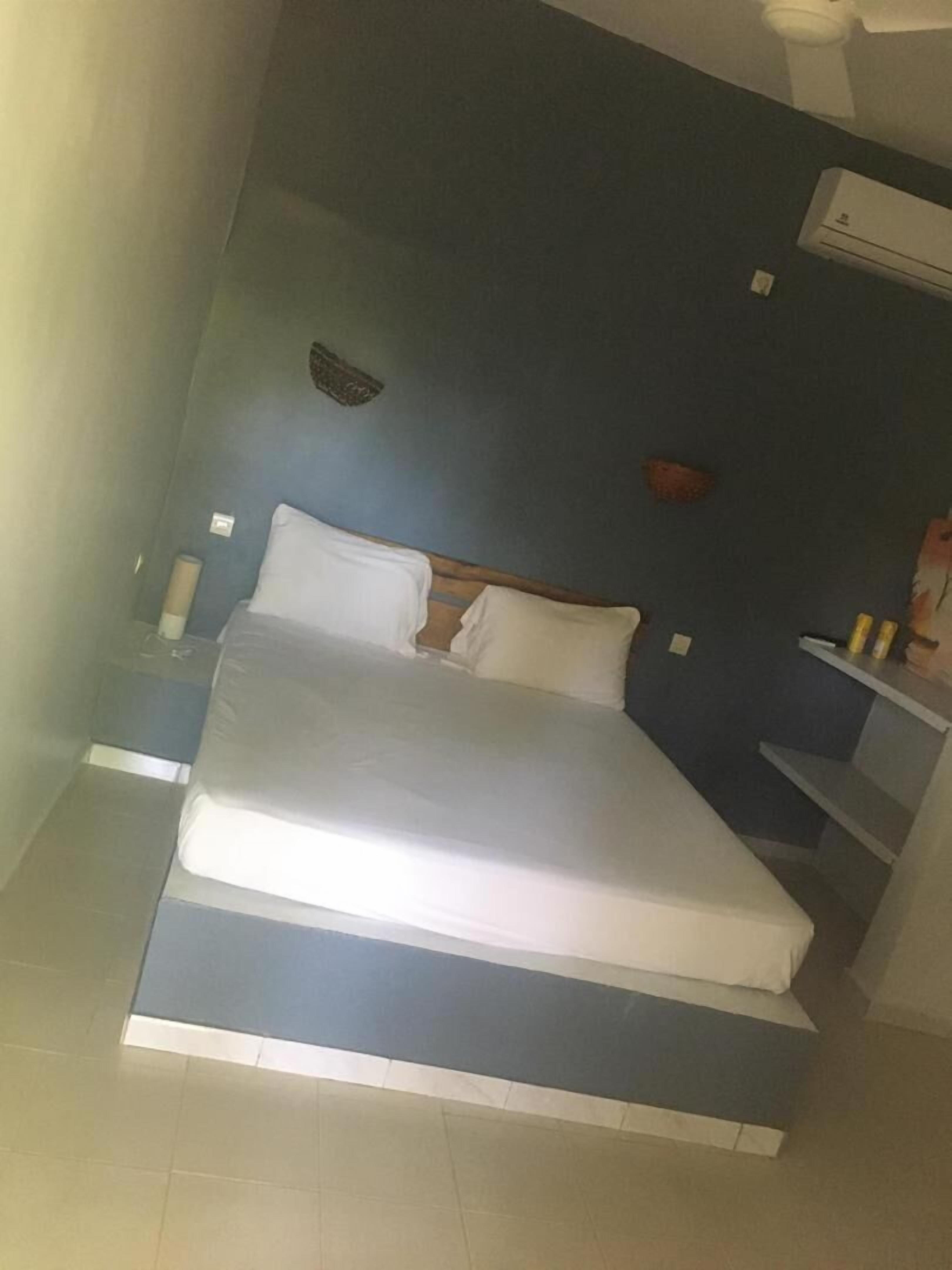 A bedroom with a bed, a nightstand, a wall-mounted air conditioner, and a small shelf with items.
