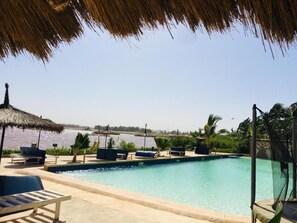A pool area with lounge chairs and a thatched roof structure.