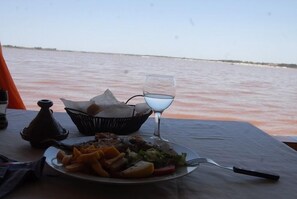A table with a plate of food, a glass of water, and a basket of bread.