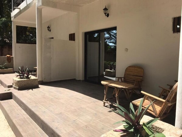 A covered outdoor area with a wooden floor, a chair, and a potted plant.