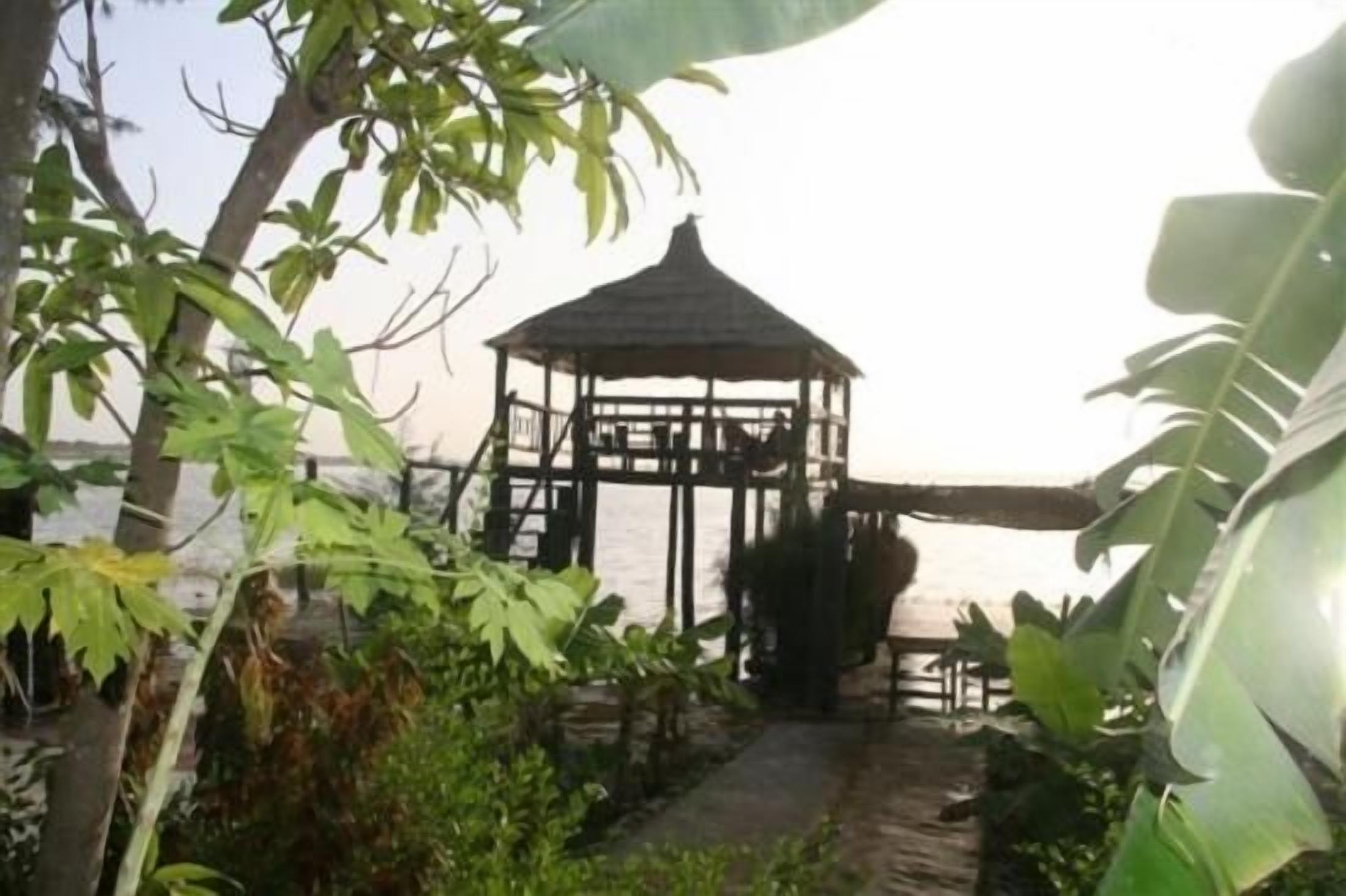 A gazebo structure with a roof, surrounded by lush greenery and a pathway leading to it.