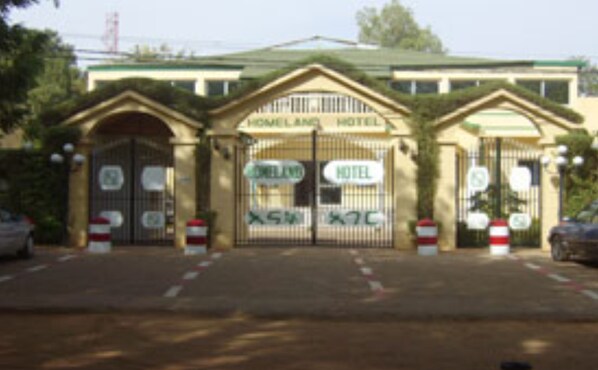 A hotel entrance with a gated driveway, a sign reading "HOMELAND HOTEL," and a sign indicating a 5-star rating. - Homeland Hotel (Niamey)
