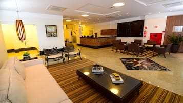 Um saguão de hotel com balcão de recepção, área de estar e uma tela grande.