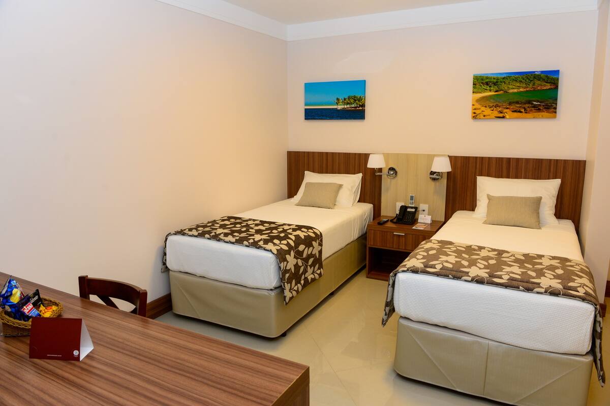 Een hotelkamer met twee bedden, een houten tafel en een klein bureau met een lamp.