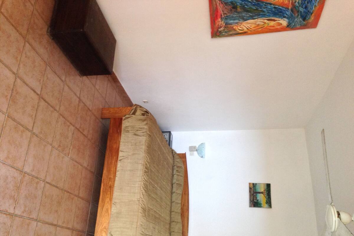 Une pièce avec un lit, un tableau au mur et un ventilateur de plafond.