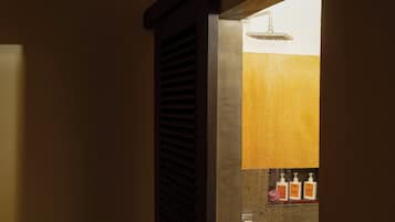 Una zona de ducha con un chorro de agua visible, una puerta de madera con listones y un estante con botellas.
