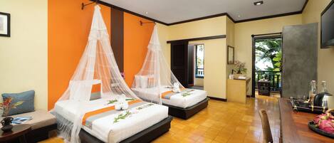 A hotel room with two beds, a small table, a chair, a TV, and a balcony with plants.