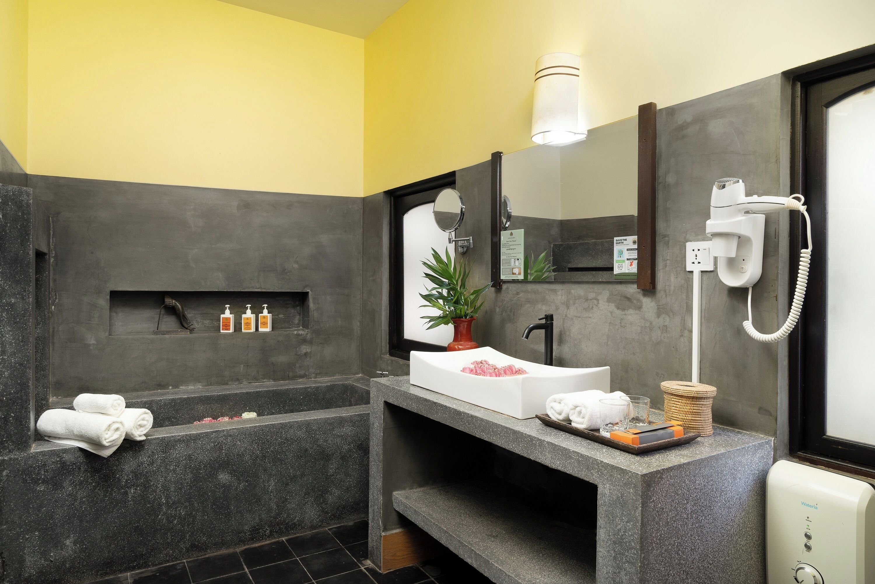 A modern bathroom with a large bathtub, a sink with a mirror, a hairdryer, and a towel rack.