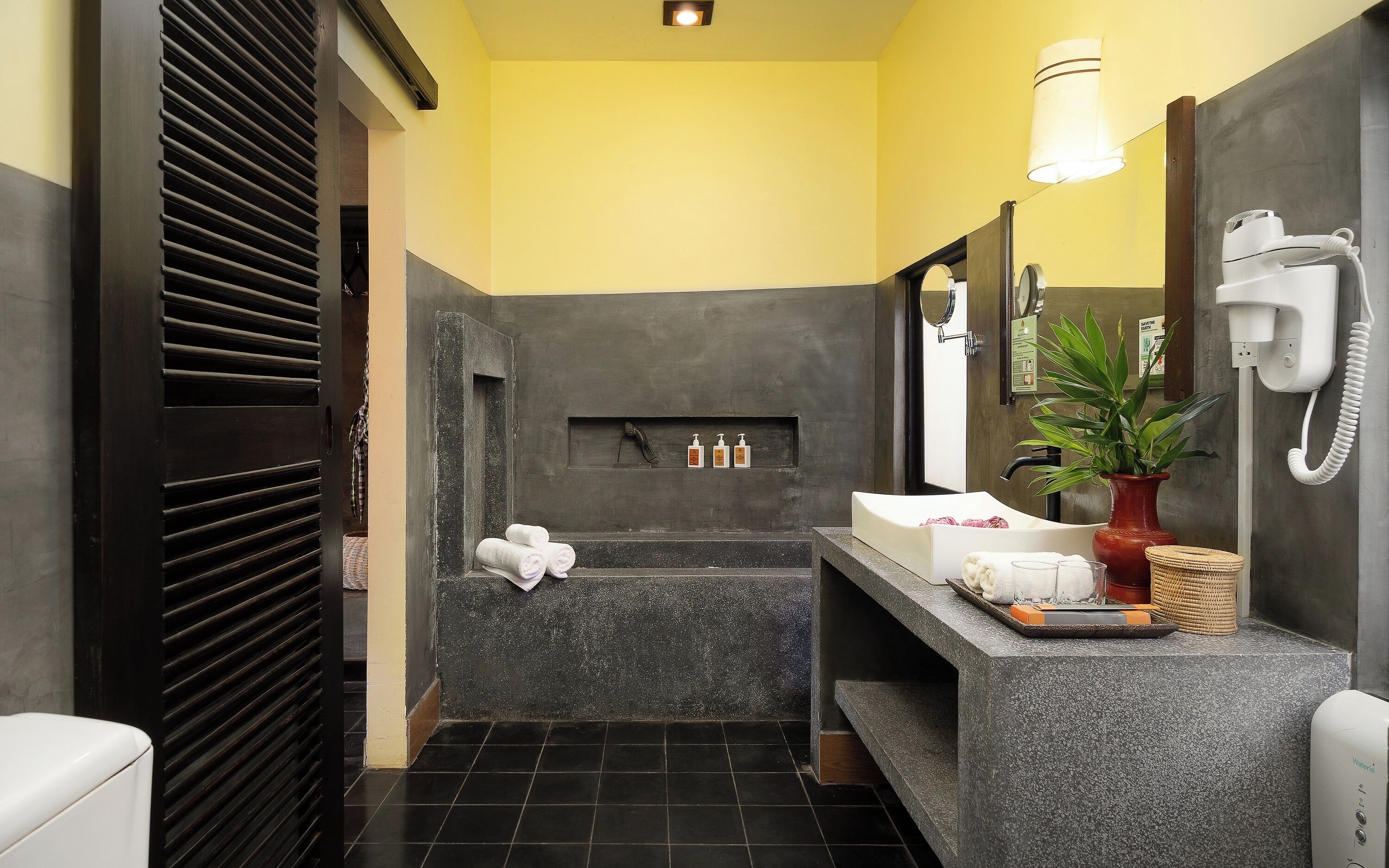 A modern bathroom with a dark tiled floor, a large mirror, a sink, and a hairdryer.