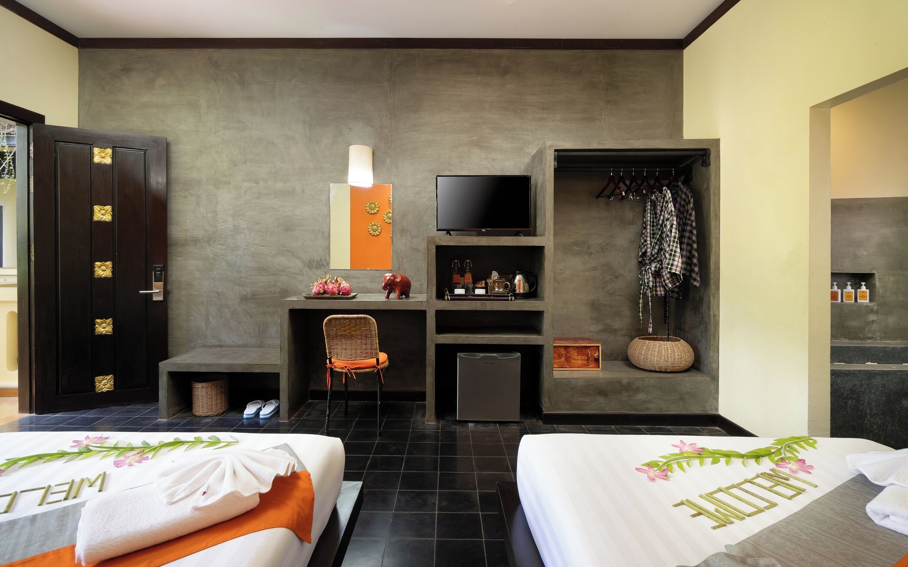 A hotel room with two beds, a television, a desk with a computer, a chair, and a wardrobe.
