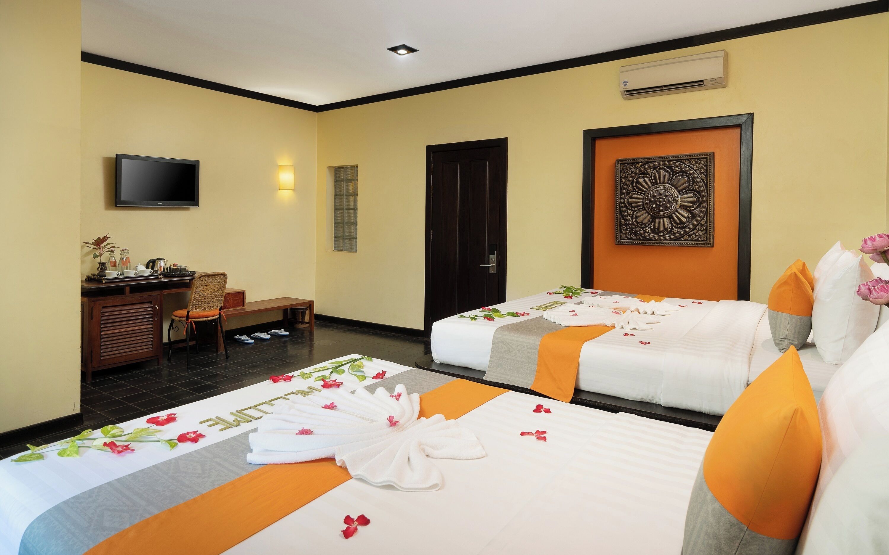 A hotel room with two beds, a desk, a chair, a TV, and a door.