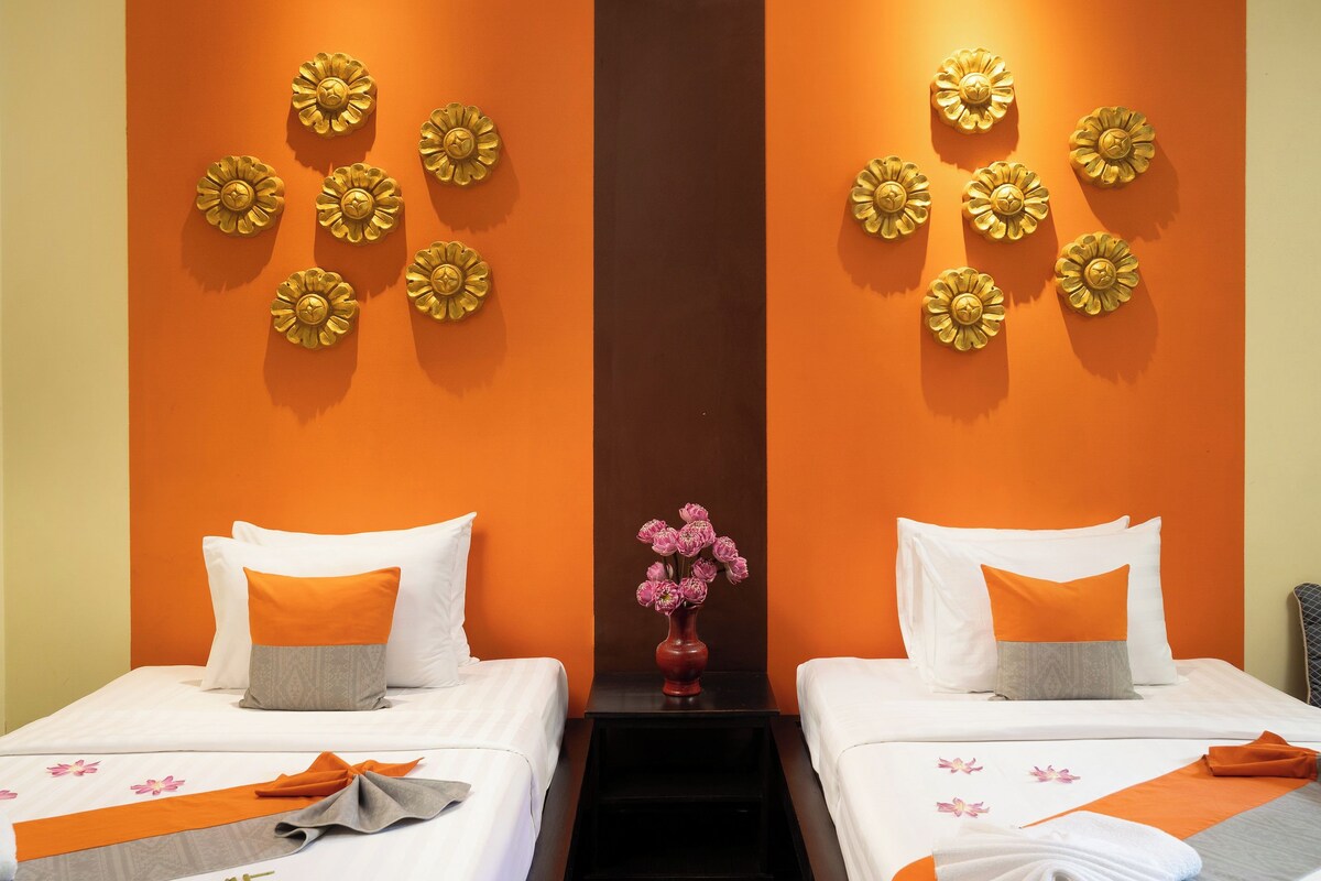 Habitación de hotel con dos camas, paredes color naranja y paneles decorativos.