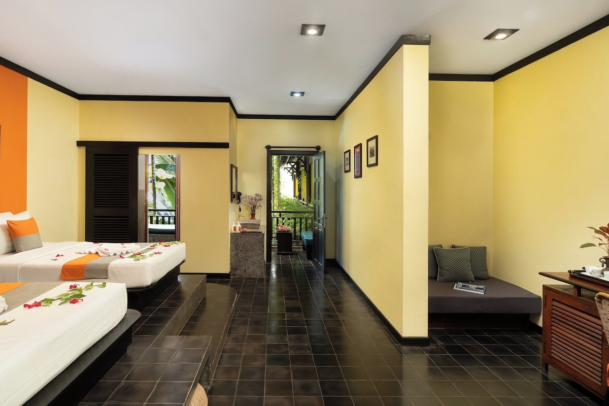 A hotel room with two beds, a small sitting area, and a view of a balcony.