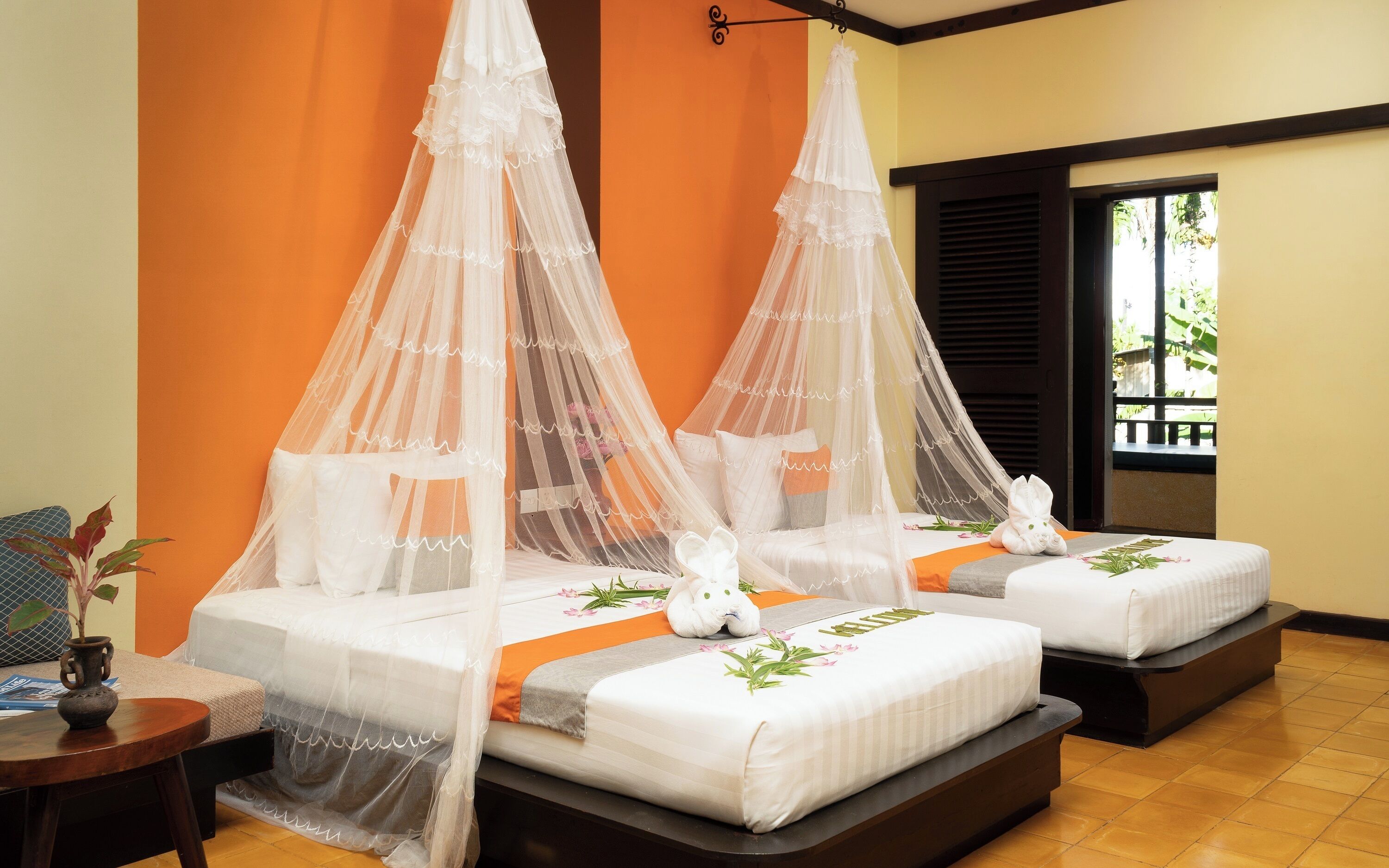 A room with two beds, each with a canopy and decorative pillows.