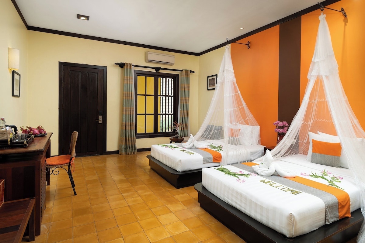 A hotel room with two beds, a desk, a chair, and a window with curtains.