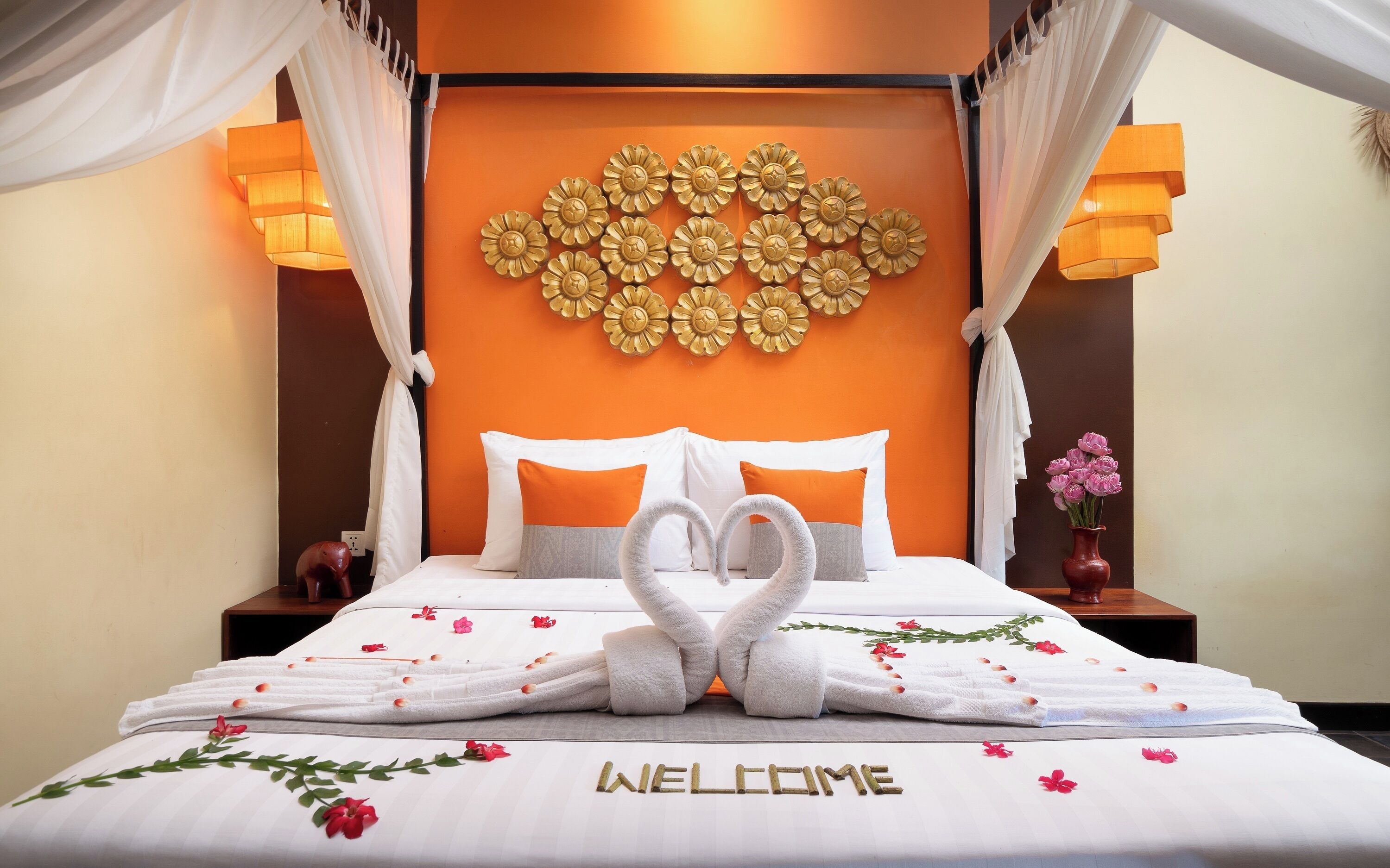 A hotel room with a bed, a decorative wall, and a welcome sign on the bed.