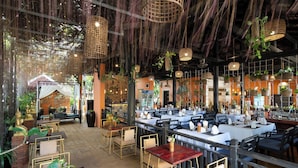 Un restaurante interior con varias mesas y sillas, cestas colgantes con plantas y una pared de ladrillo al fondo.
