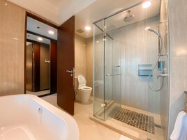 A modern bathroom with a glass-enclosed shower, a white bathtub, and a toilet.