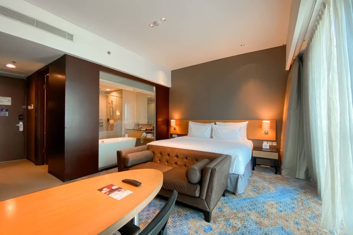 A hotel room with a large bed, a seating area with a table, a bathroom with a bathtub, and a large mirror.